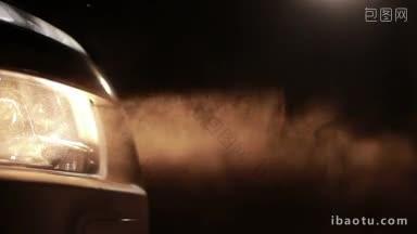尘土中黄色的汽车大灯，夜晚在乡村土路上行驶的汽车的明亮大灯